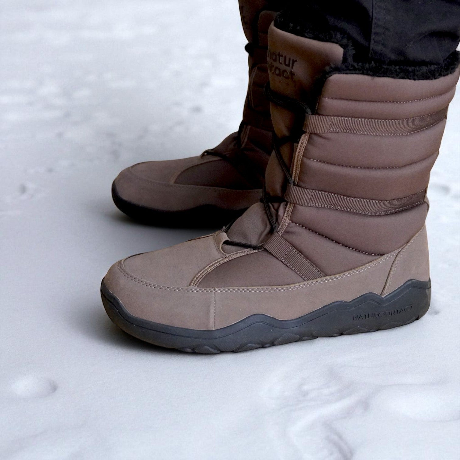 Side view of brown Naturcontact winter boots on snow, highlighting the brand logo on the sole and the layered padded structure
