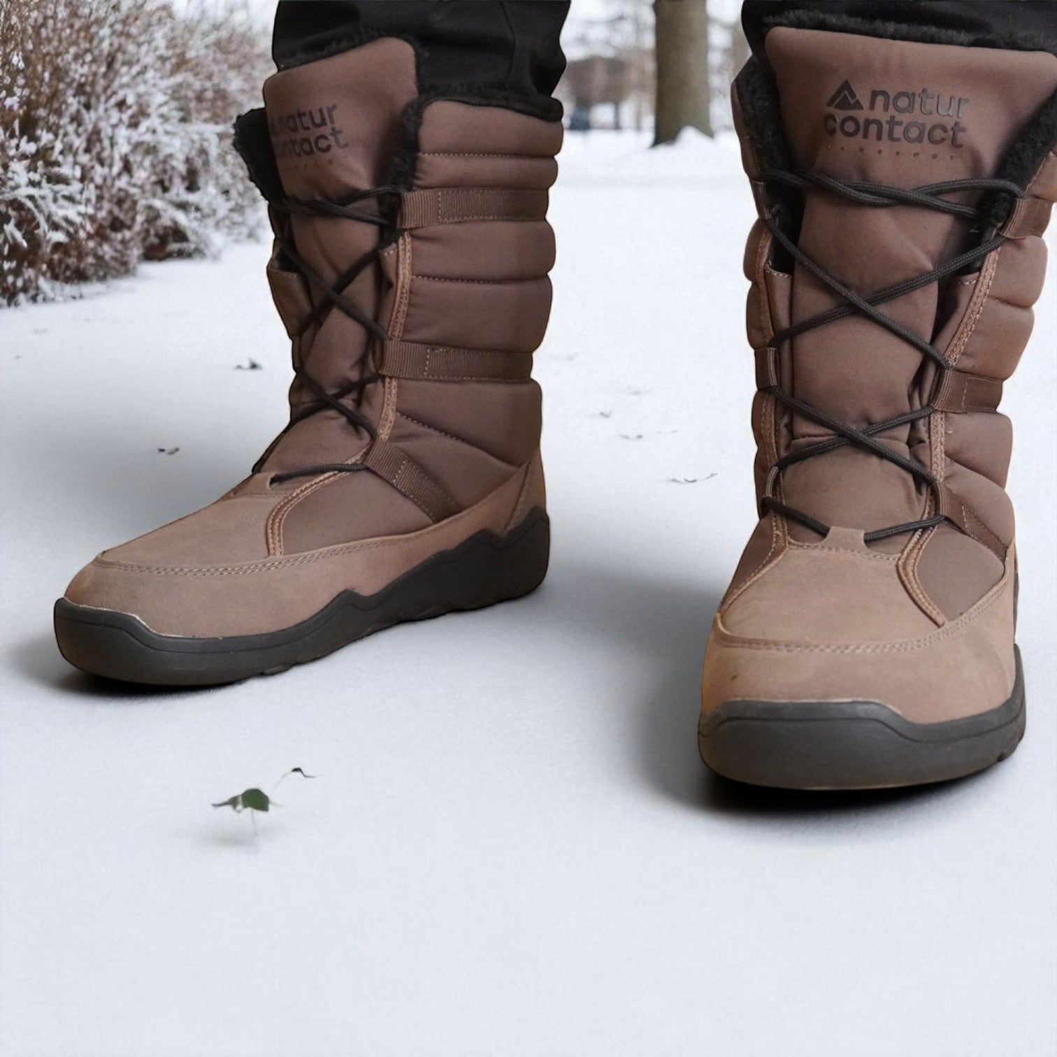 Pair of brown Naturcontact winter boots worn on snow, featuring black laces, padded upper, and rugged soles for winter grip