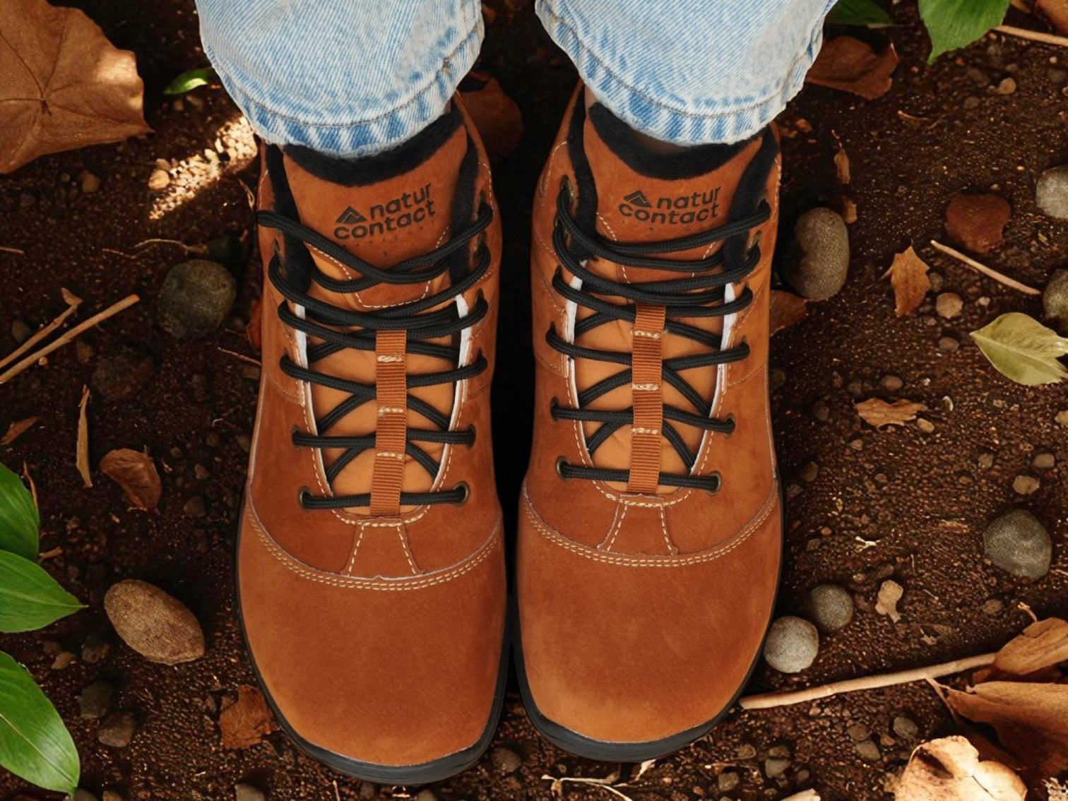 Brown hiking boots with black laces worn on a natural ground surface.