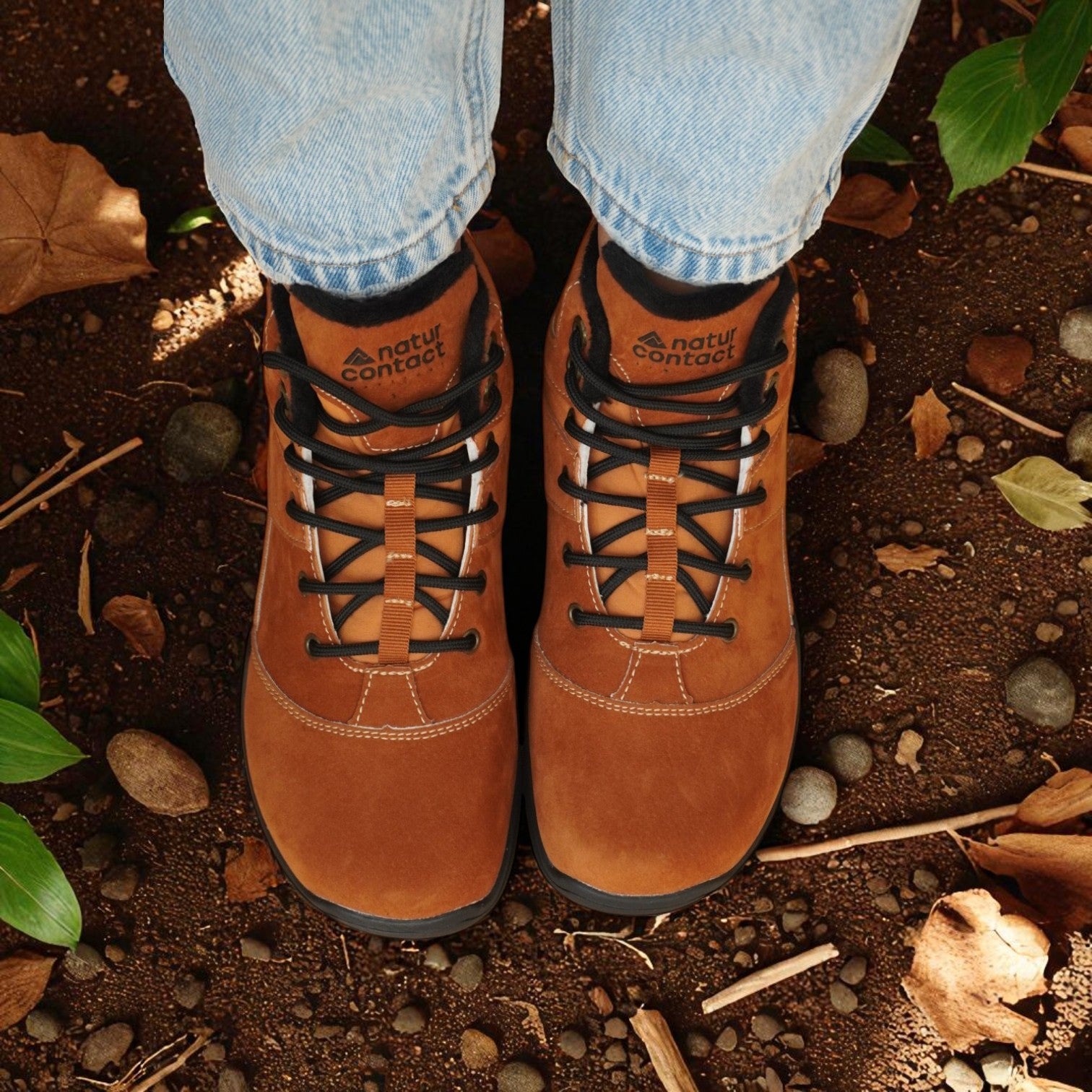 Brown hiking boots with black laces worn on a natural ground surface.