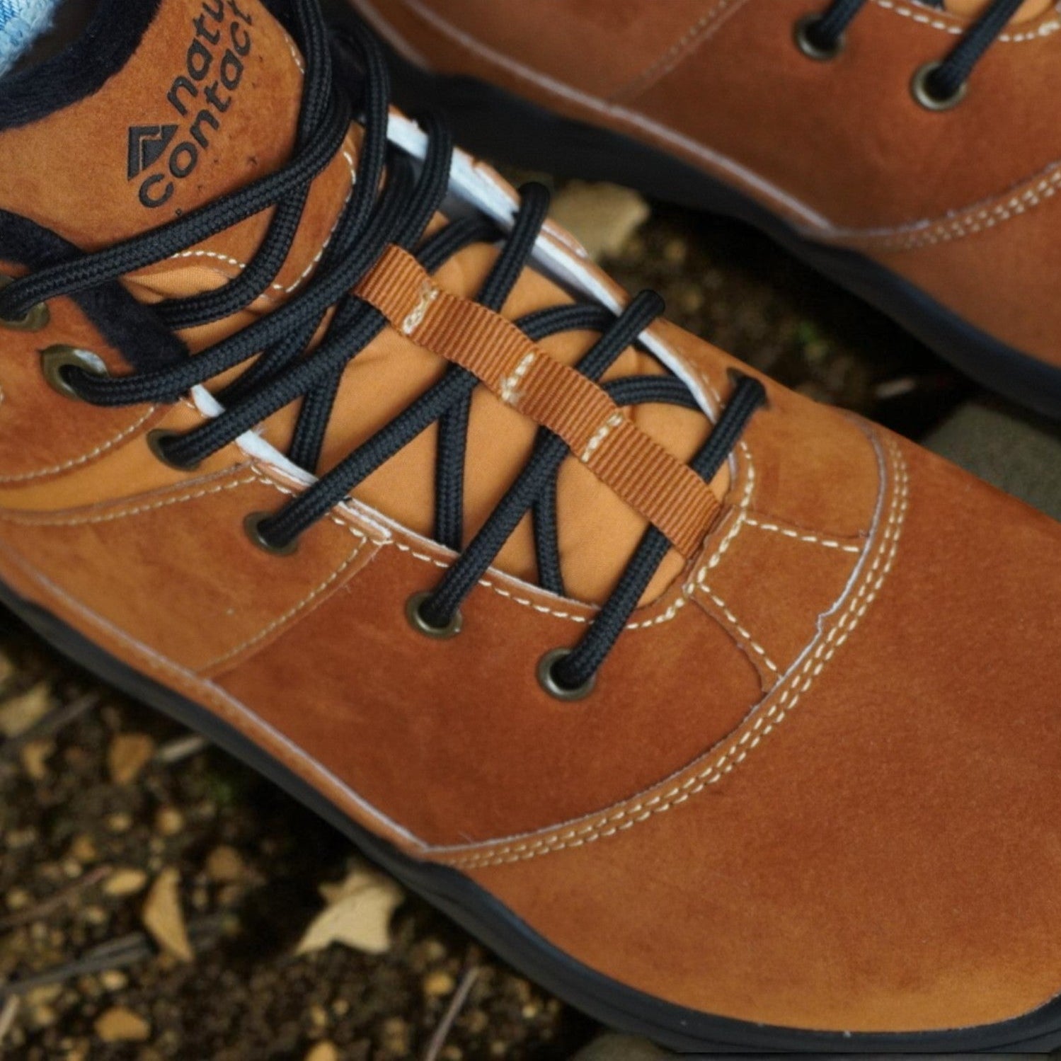 Close-up of brown leather boots with black laces on a natural ground background