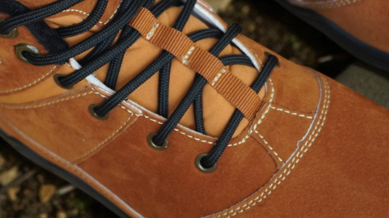 Close-up of brown hiking boots with black laces on a natural ground background