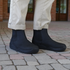 Person wearing navy ankle barefoot boots on a paved surface with beige pants.