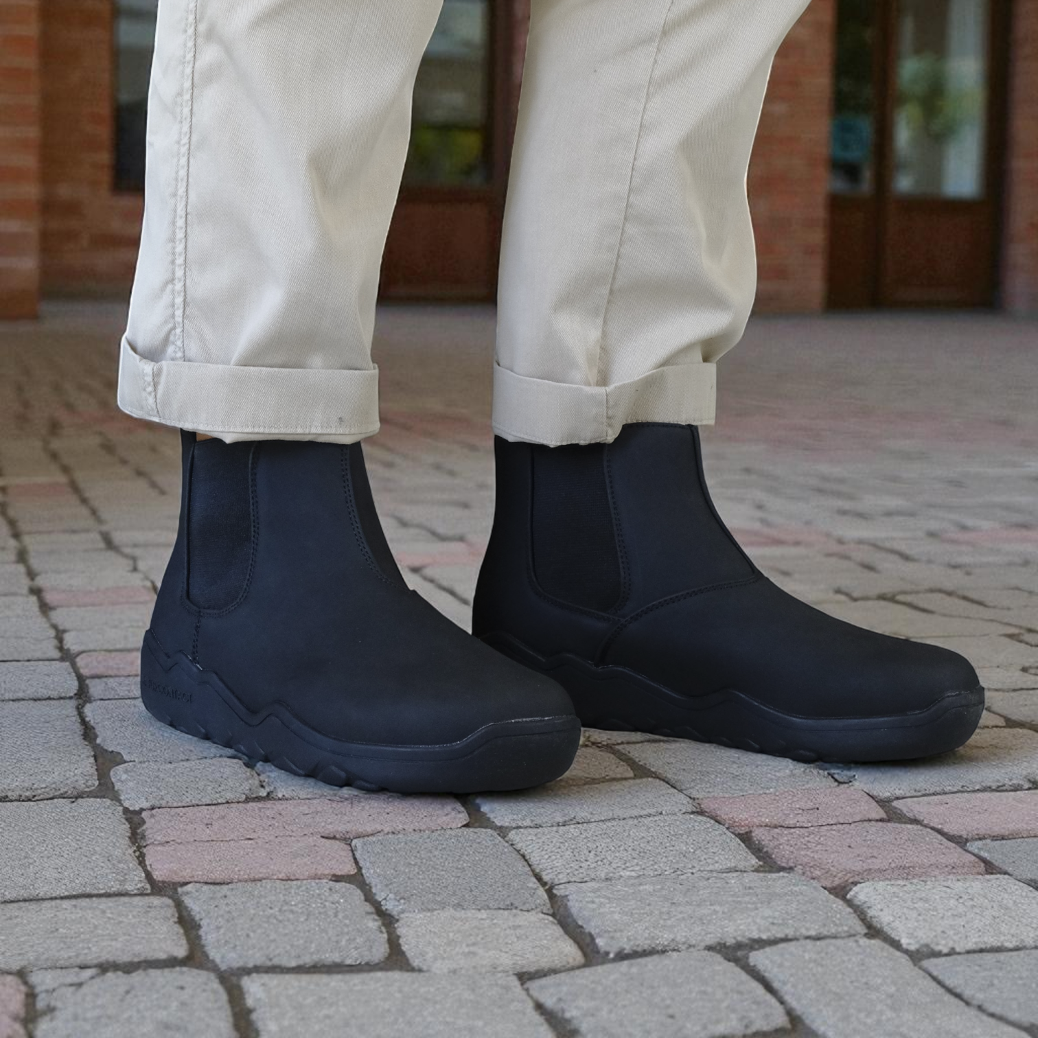 Person wearing navy ankle barefoot boots on a paved surface with beige pants.