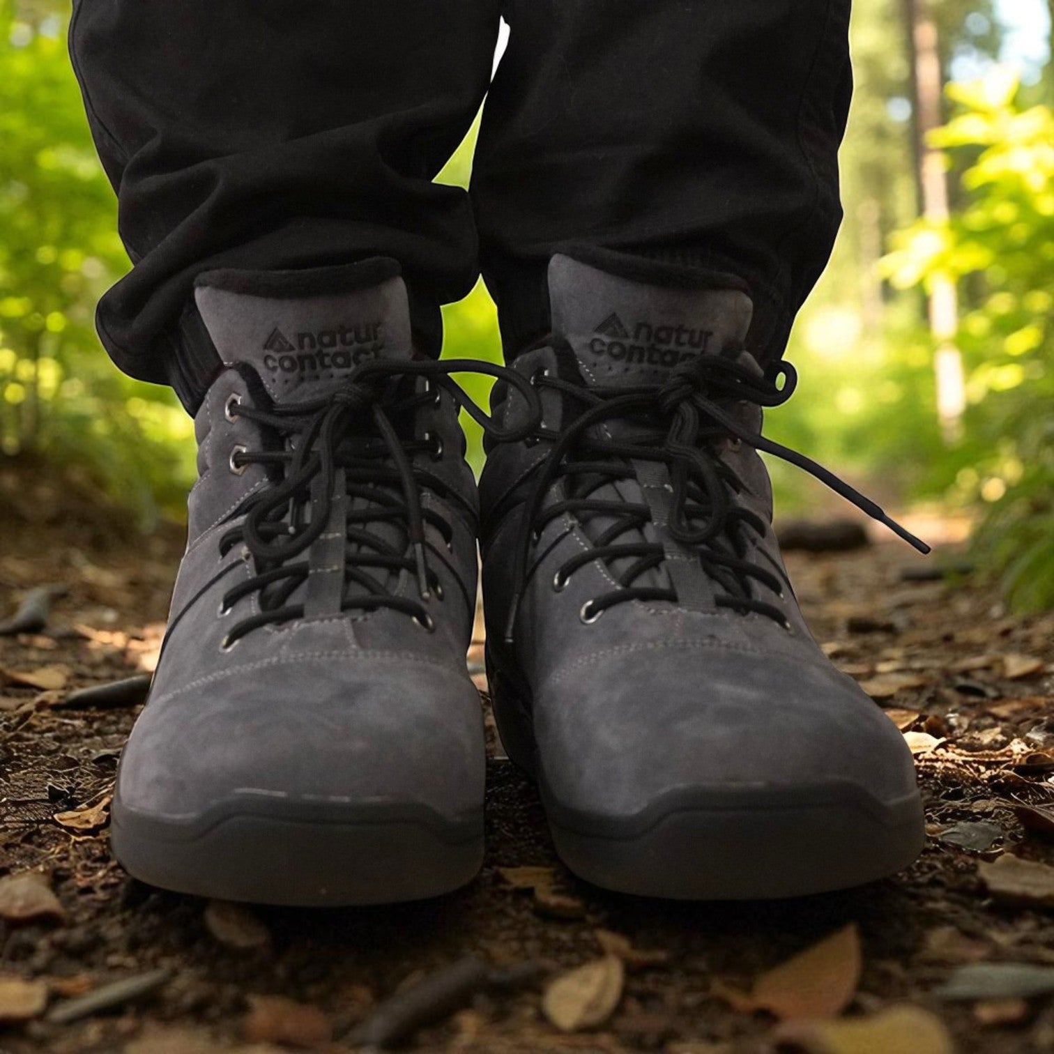 Front view of grey Naturcontact outdoor boots on a forest trail, featuring black laces, metal eyelets, and a rugged sole