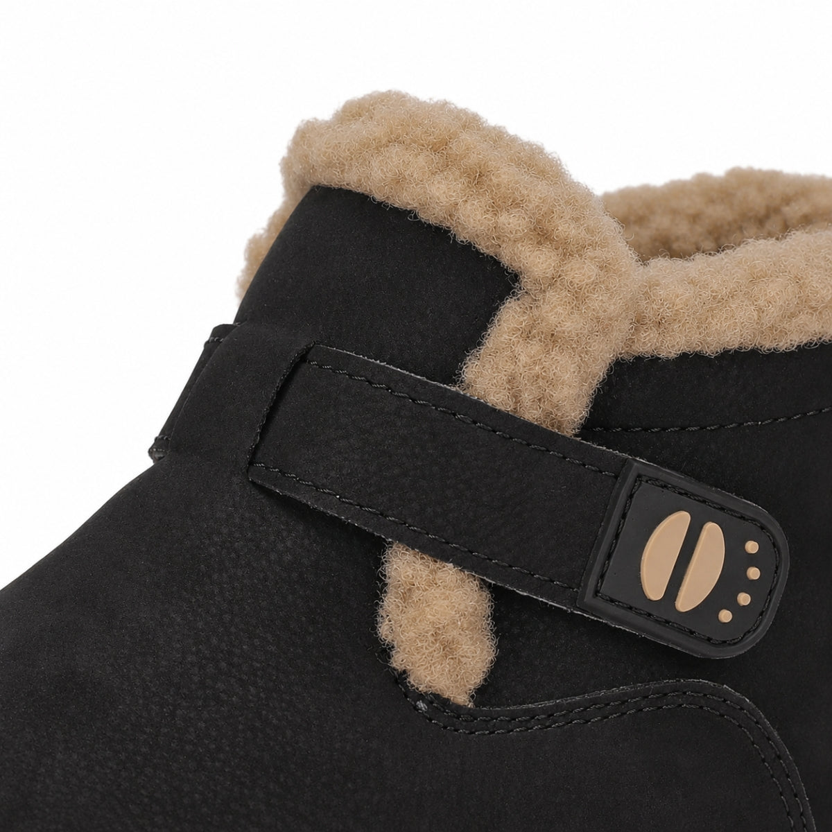 Close-up of a black suede ankle boot with a tan shearling lining and a black strap closure featuring a tan paw-print detail, shown on a white background.